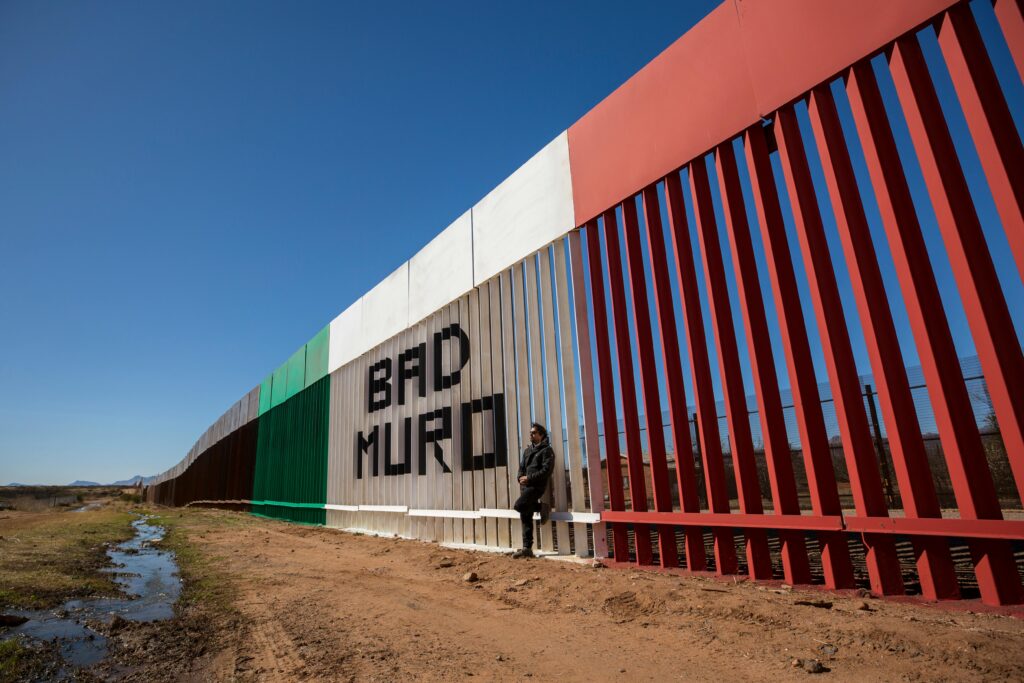 pexels-photo-12330156-12330156-1 Image of a man standing by the border wall painted with Mexican flag colors in Naco, Sonora, Mexico.